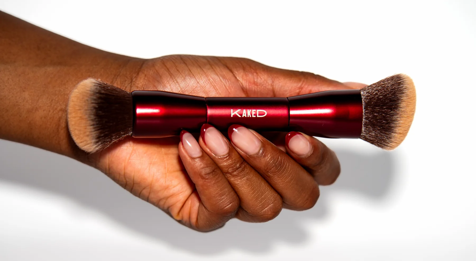A hand holding a red Kaked duo brush, shot by EchoHaus
